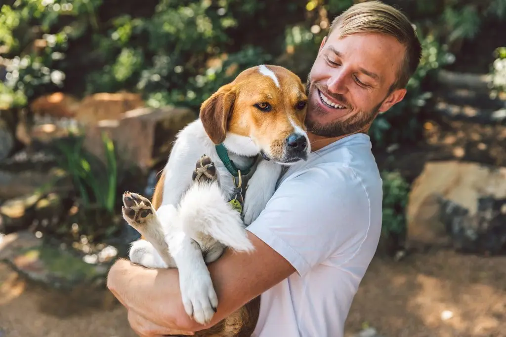 Man holding medium sized dog in arms and smiling