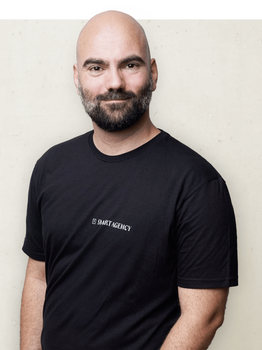 Porträtfoto eines Mitarbeiters von Smart Agency, lächelnd mit einem Smart Agency T-Shirt vor einem neutralen Hintergrund.