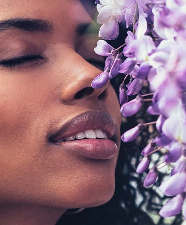 Thoughtful happy young black woman with dark curly hair smelling lavender flowers with eyes closed