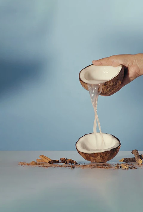 A hand pouring coconut water from one coconut half to another