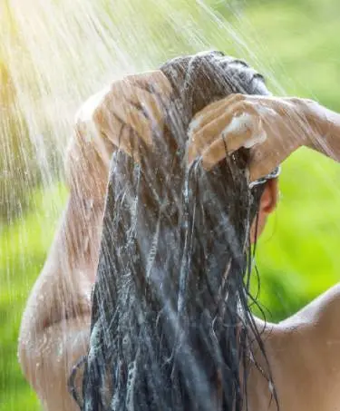 Back of dark-haired woman showering outdoors using a tea tree oil conditioner