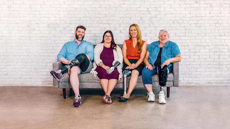 Four people sitting on a bench. A man with a below the knee prosthetic leg, a woman with a bebionic hand, a woman with a C-Leg prosthetic knee joint and a woman with a trans-tibial prosthesis.