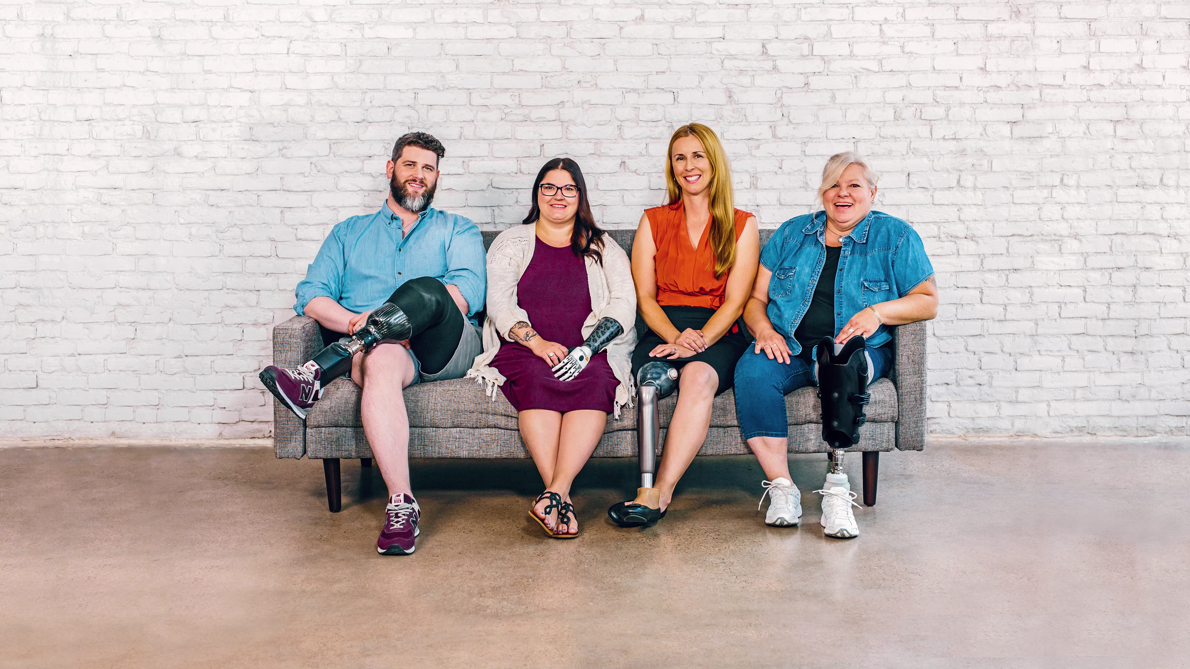 Four people sitting on a bench. A man with a below the knee prosthetic leg, a woman with a bebionic hand, a woman with a C-Leg prosthetic knee joint and a woman with a trans-tibial prosthesis.