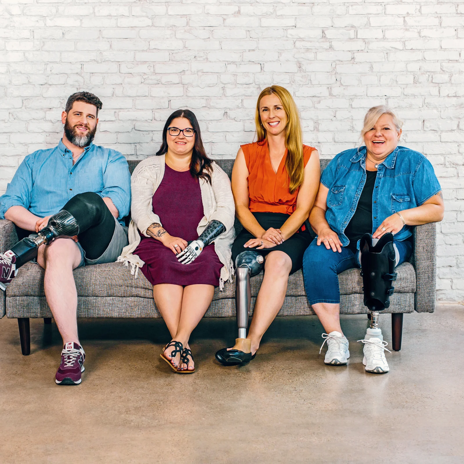 Four people sitting on a bench. A man with a below the knee prosthetic leg, a woman with a bebionic hand, a woman with a C-Leg prosthetic knee joint and a woman with a trans-tibial prosthesis.