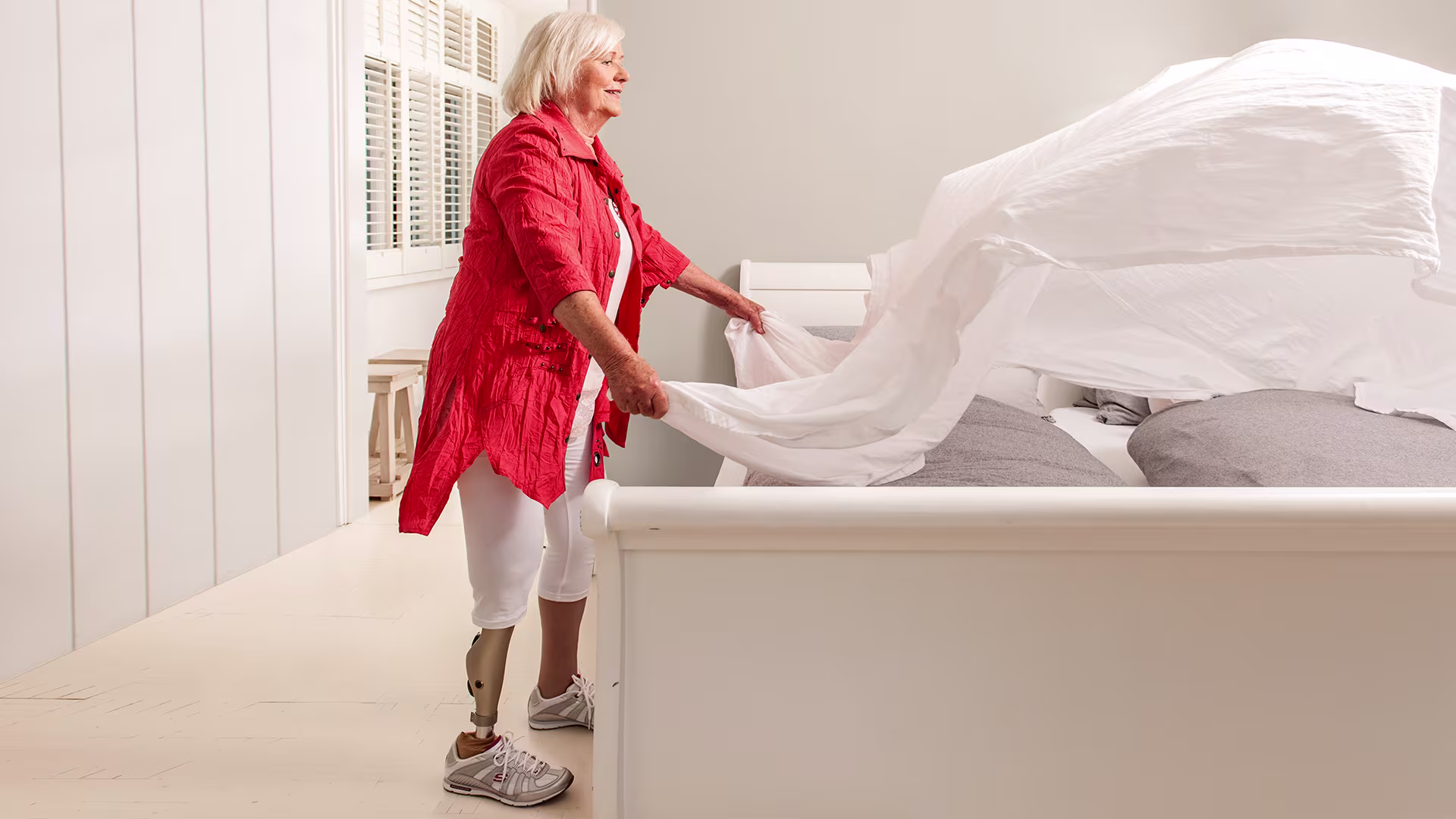 Женщина на протезе бедра с коленным модулем Kenevo заправляет кровать.