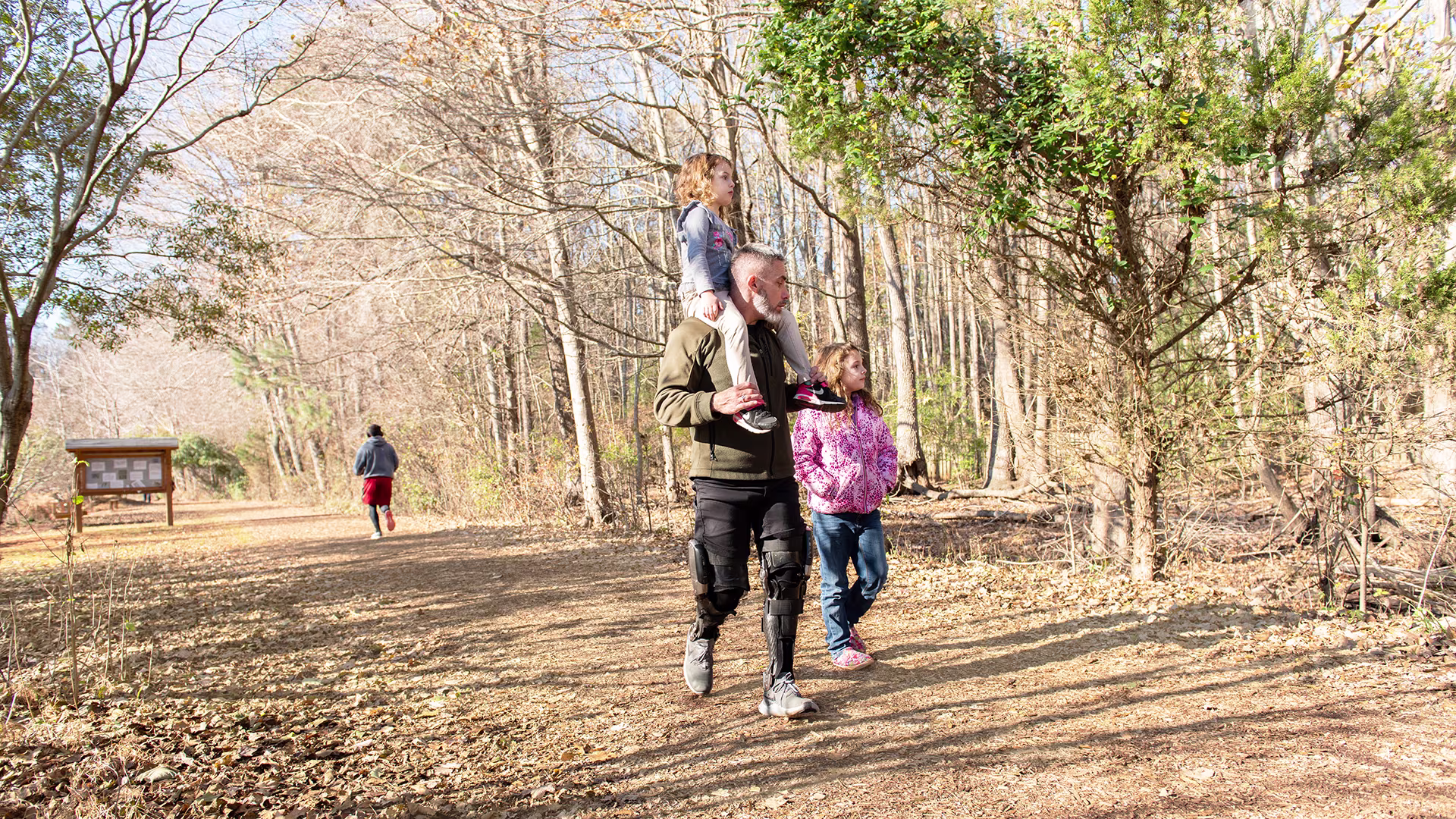 A family of three walking on an outdoor trail. The father holds his daughter on his shoulders without strain thanks to his custom-made Ottobock C-Brace