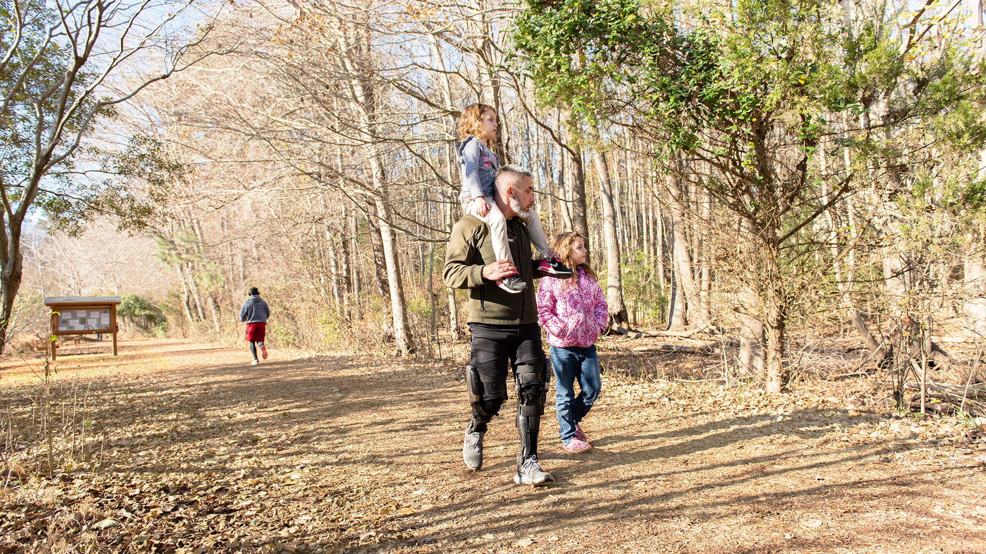 A family of three walking on an outdoor trail. The father holds his daughter on his shoulders without strain thanks to his custom-made Ottobock C-Brace