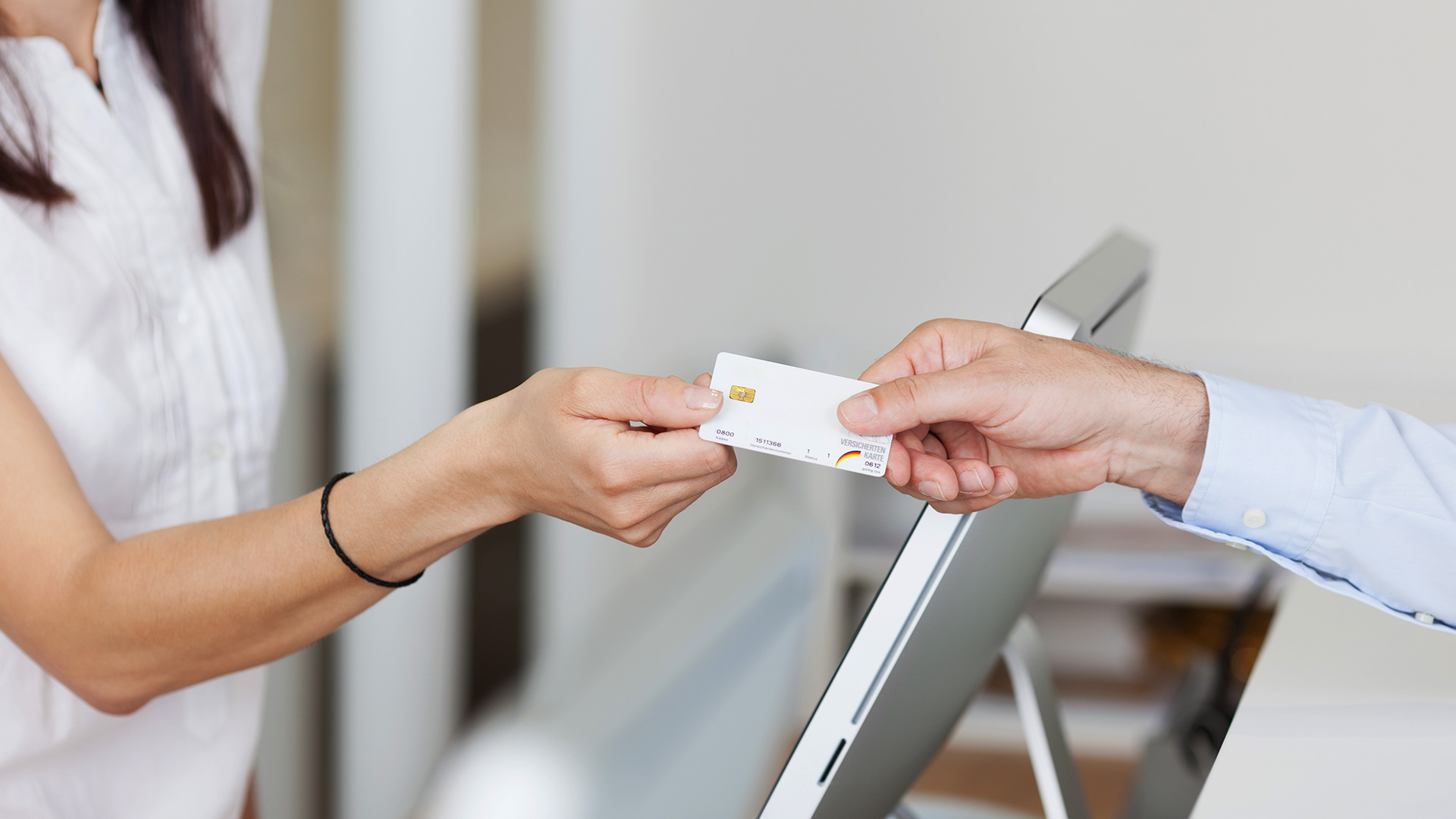 Female patient hands her insurance card to the receptionist at a medical clinic.