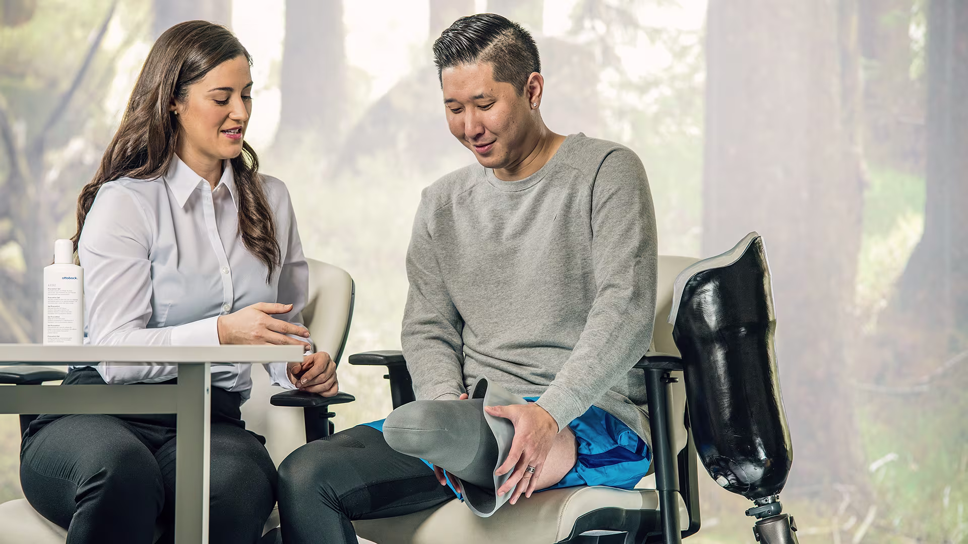 Prosthetist sitting at a table and talking to a leg amputee who shows his residual limb with a liner on