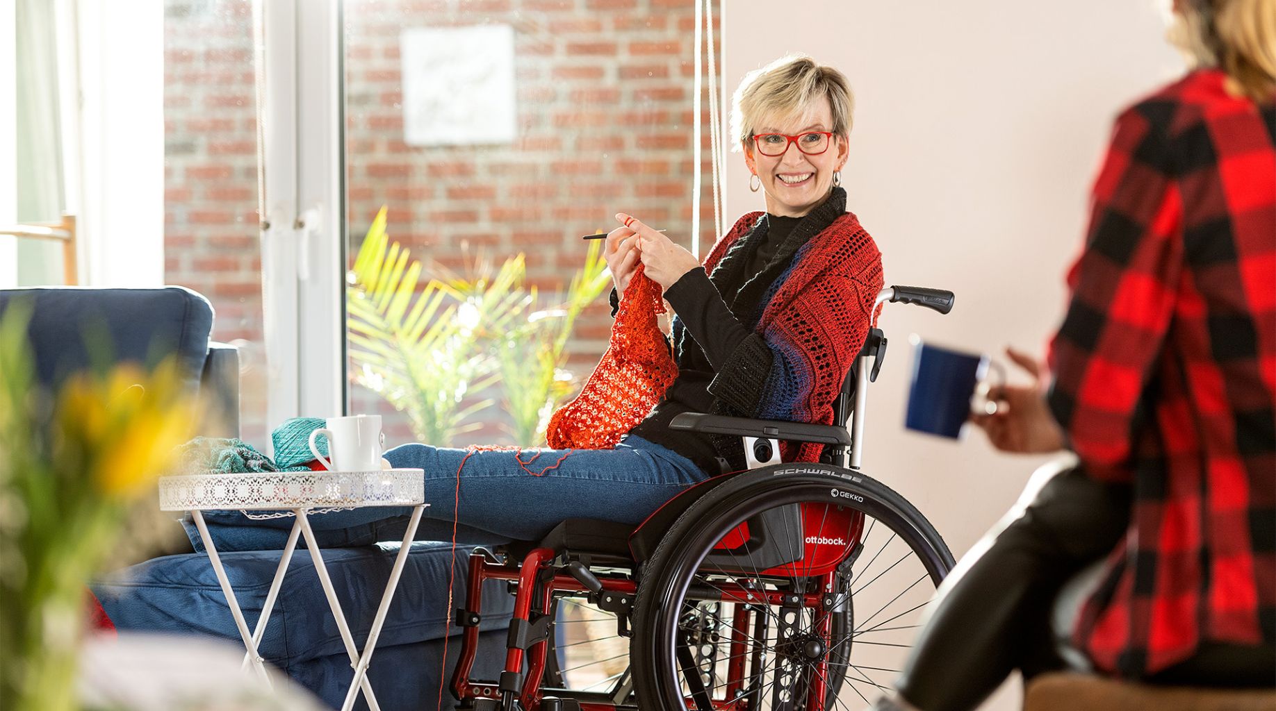 Kobieta siedzi na wózku i szydełkuje.