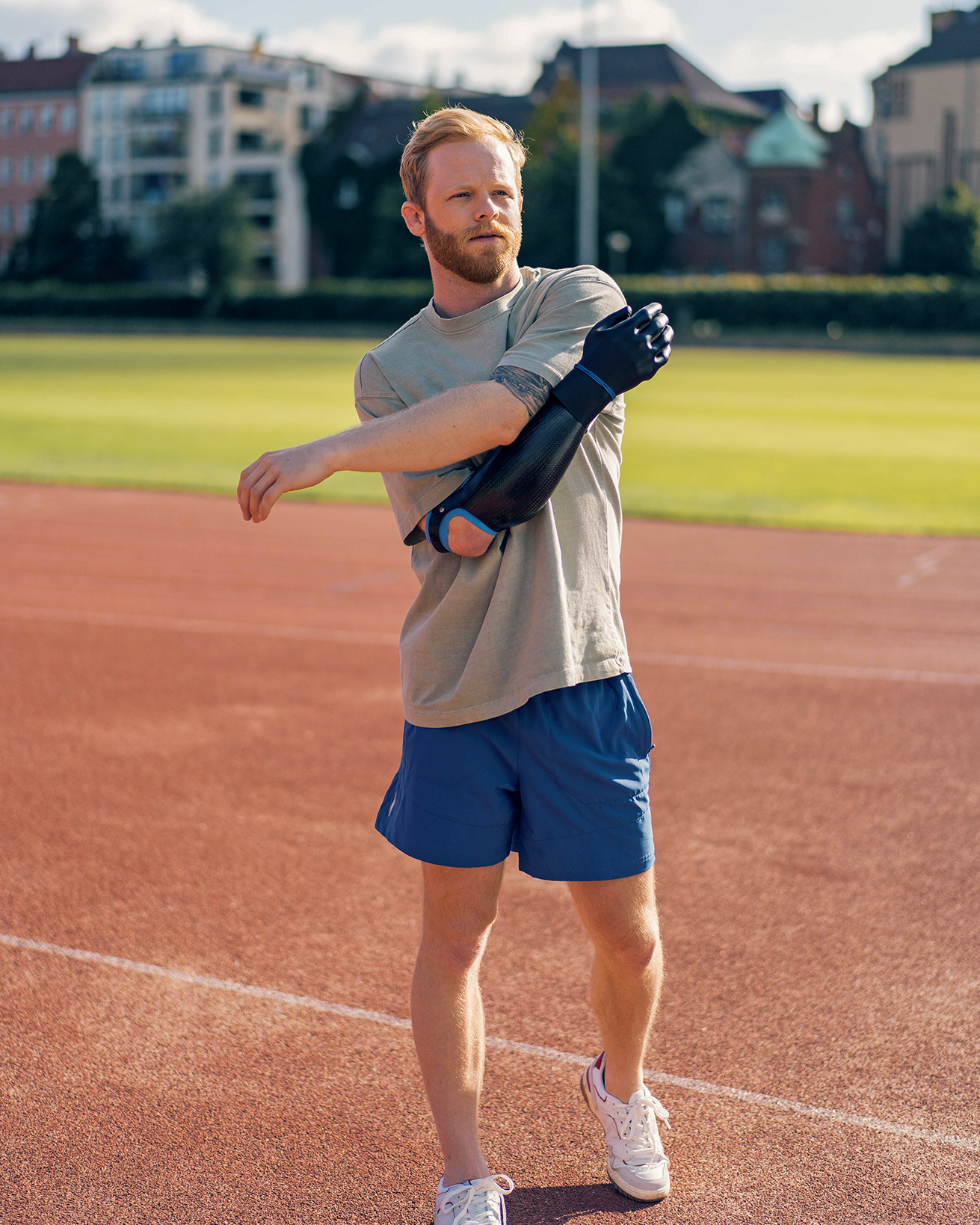 A man with a black Michelangelo multi-grip prosthetic hand stretches his sound side across his body while he stands on a running track 