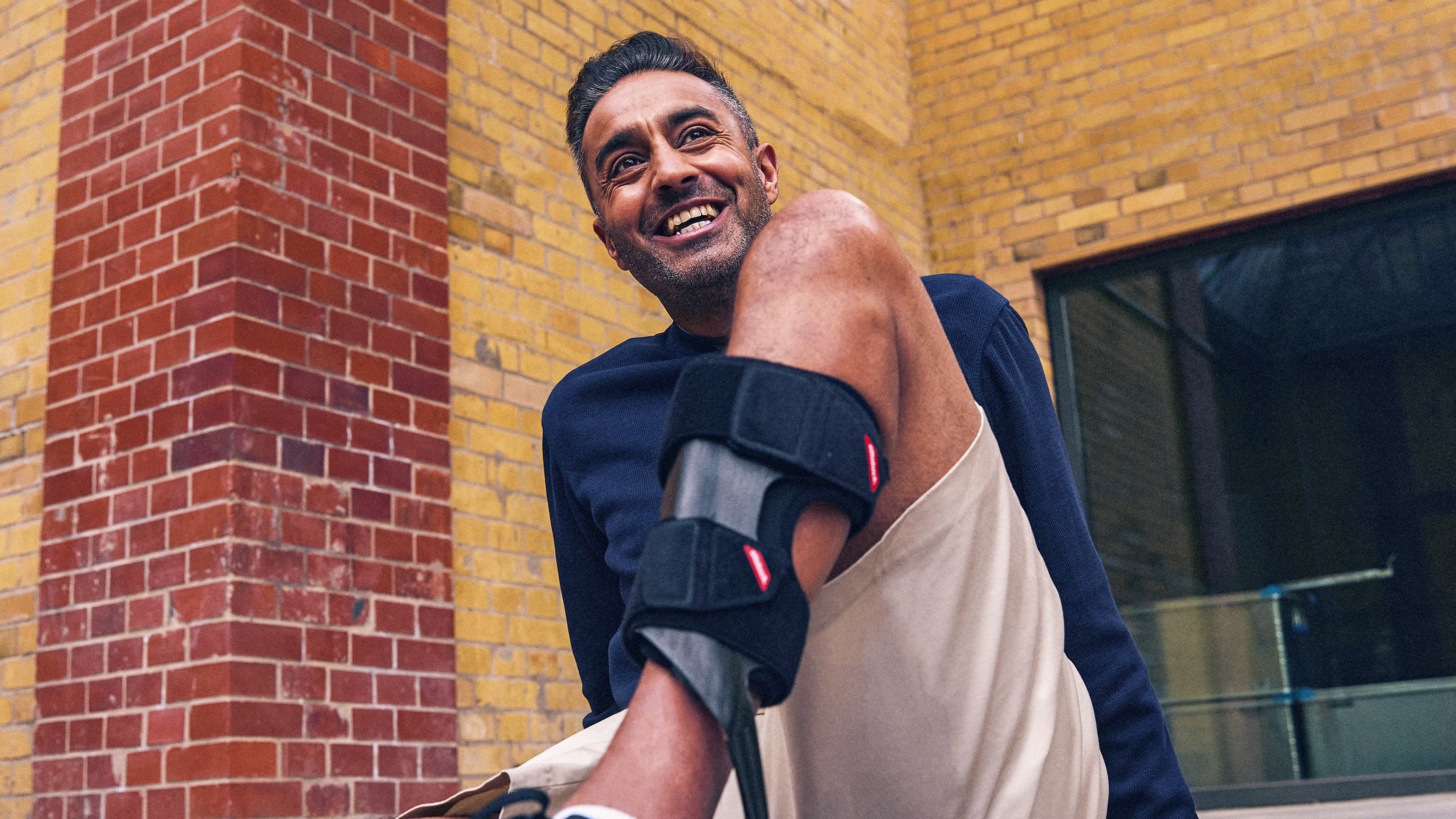 Smiling man with lower leg orthosis in front of a brick wall.