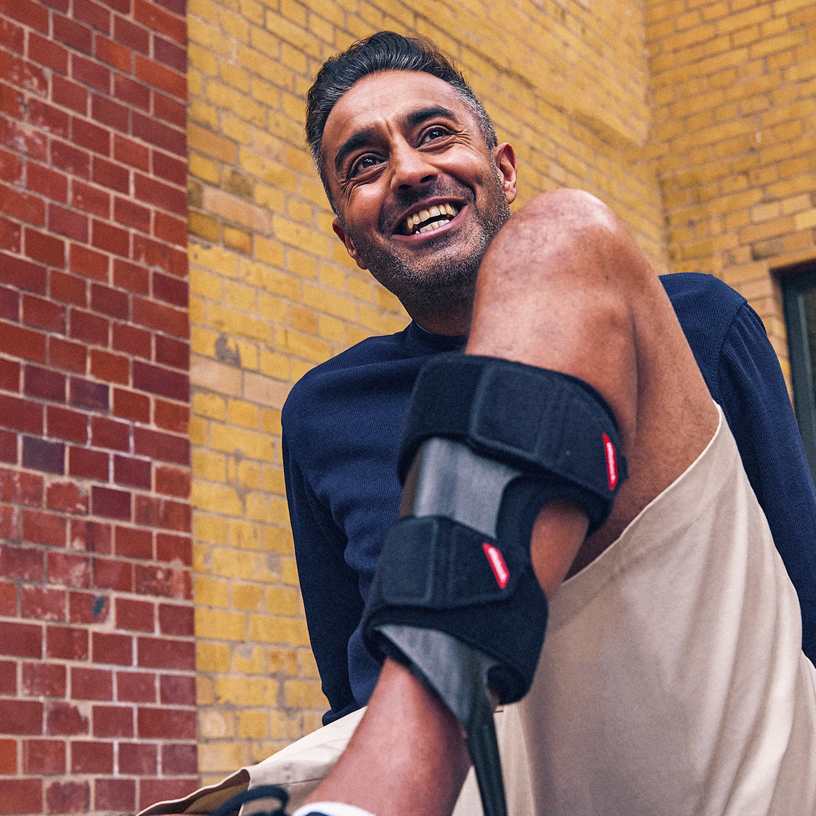 Smiling man with lower leg orthosis in front of a brick wall.