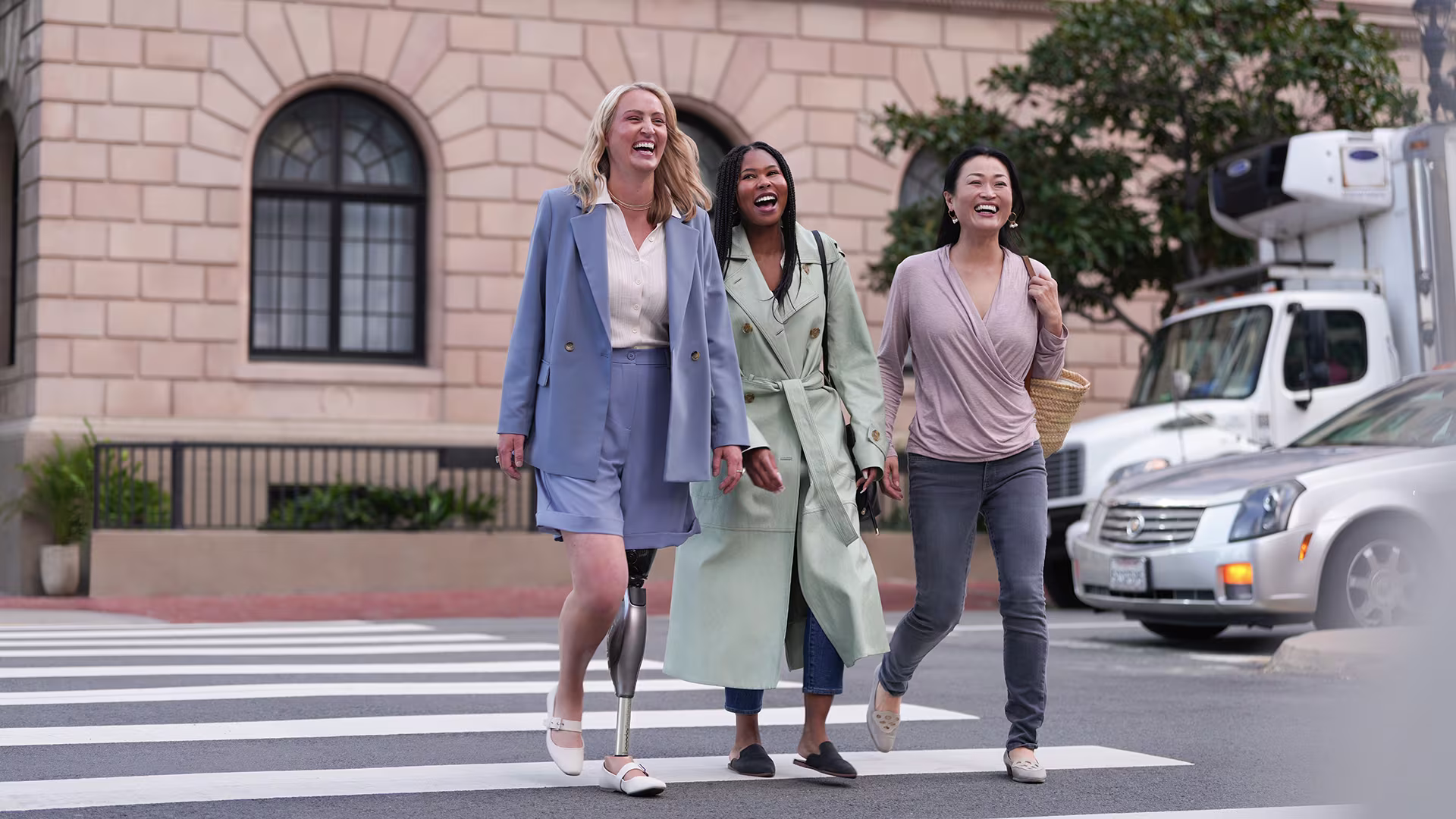 3 junge Frauen laufen gemeinsam über einen Zebrasteifen und lachen dabei. Eine von Ihnen trägt das mechatronische Kniegelenk Genium X4 von Ottobock.