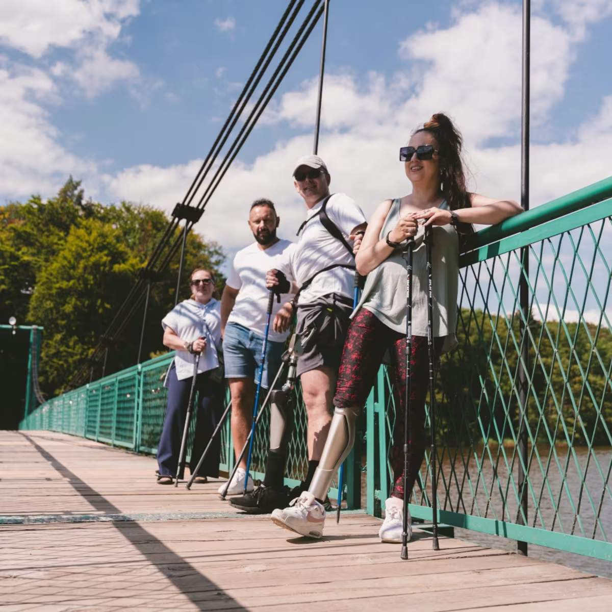 Grupa ludzi po amputacji stoi na moście z kijkami nordic-walking