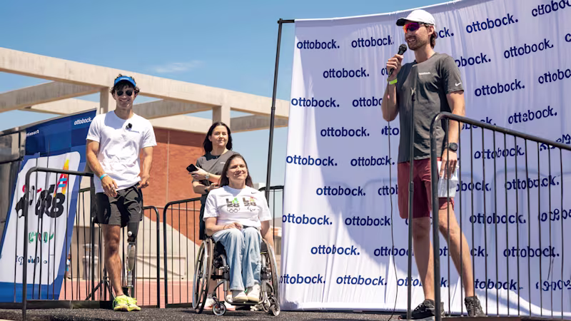 Clinical Specialist Lucas Crisanti on stage with a microphone in front of an Ottobock banner with three smiling onlookers waiting their turn to speak