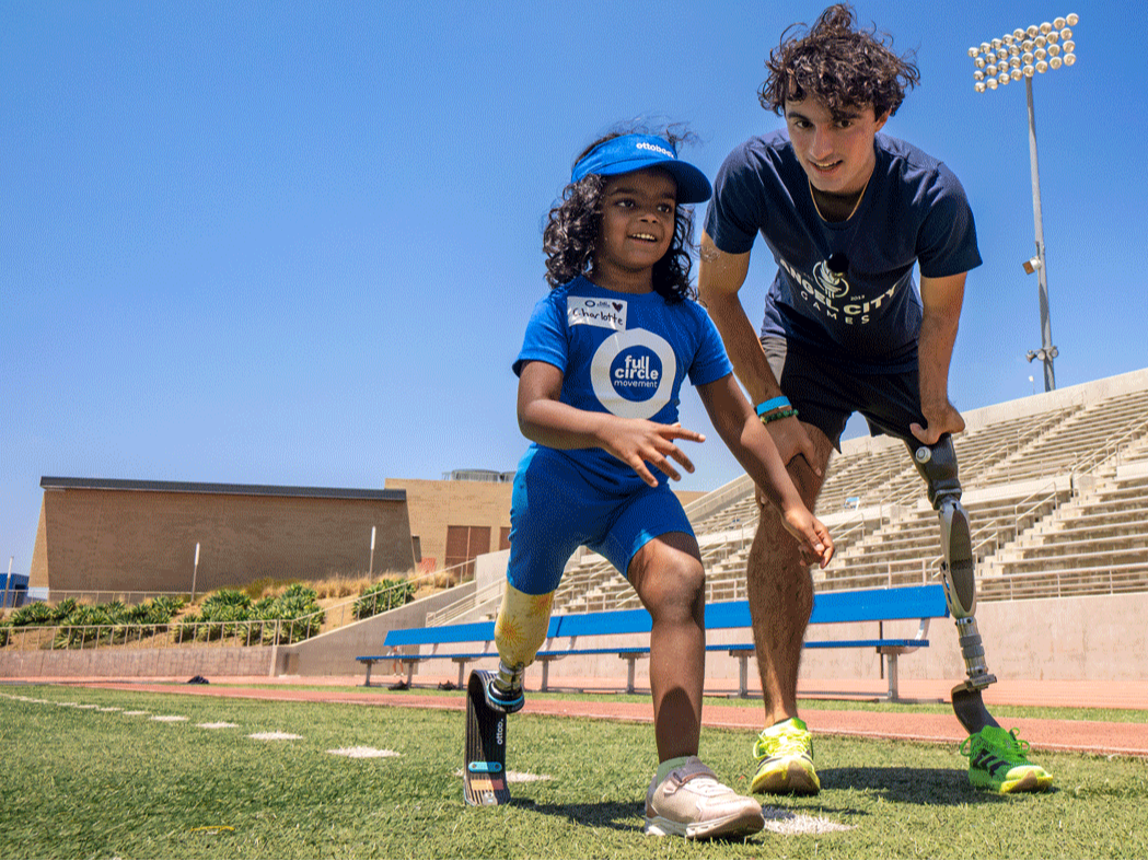 Paralympian with prosthetic leg coaching young girl who also has a prosthetic leg how to run