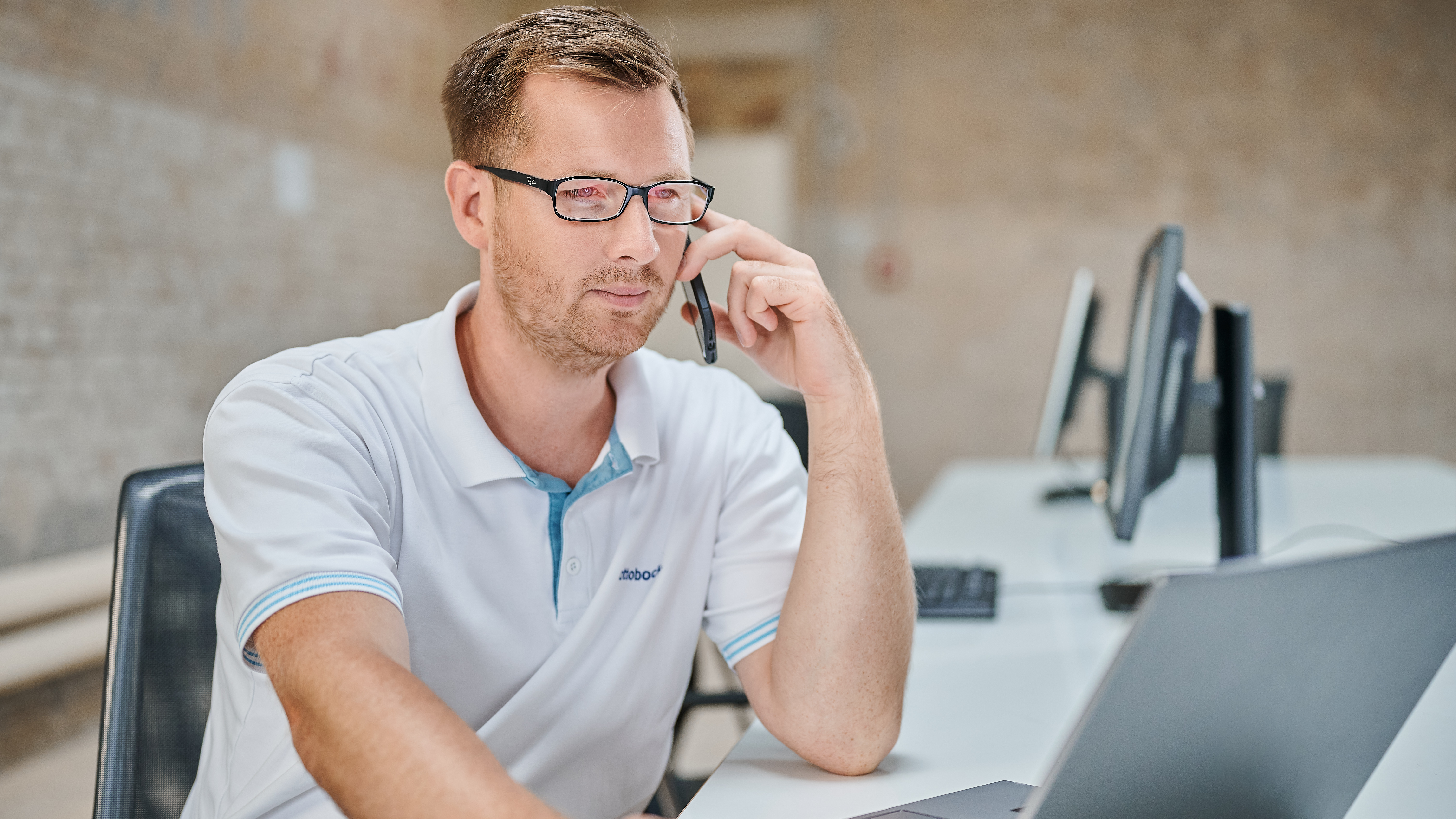 An orthopaedic technician is talking on the phone while looking at a laptop screen.