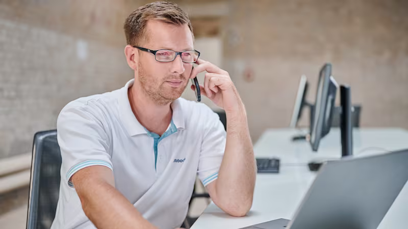 An orthopaedic technician is talking on the phone while looking at a laptop screen.