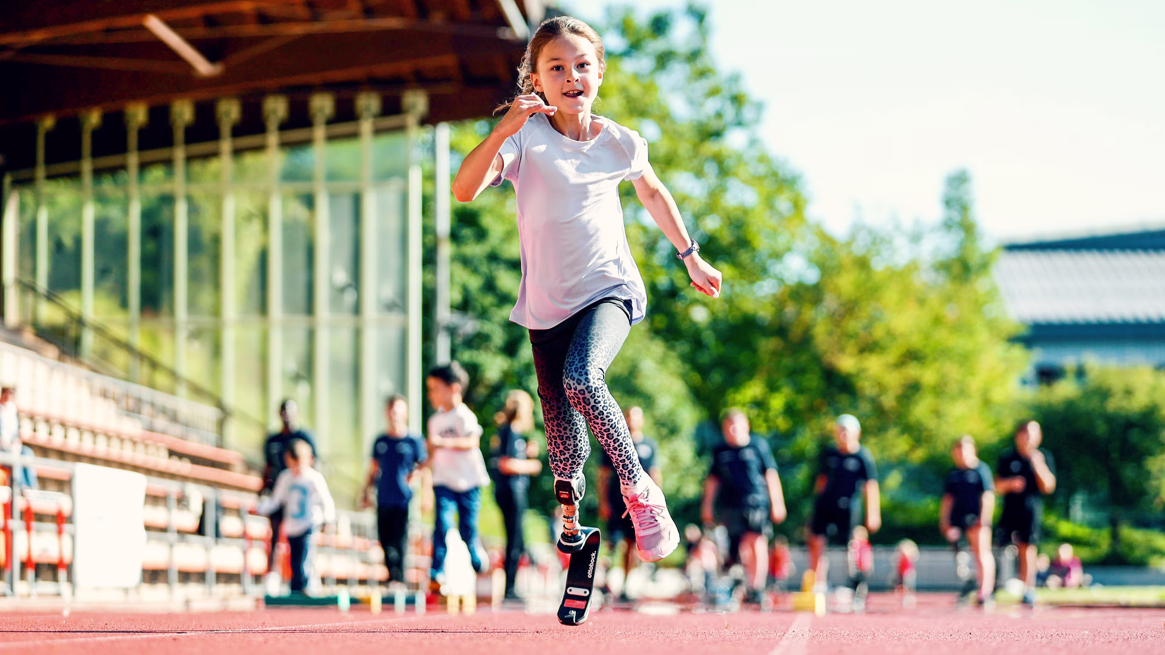 Ein kleines Mädchen mit Beinprothese und Sportfeder Ottobock läuft lachend über einen Sportplatz.