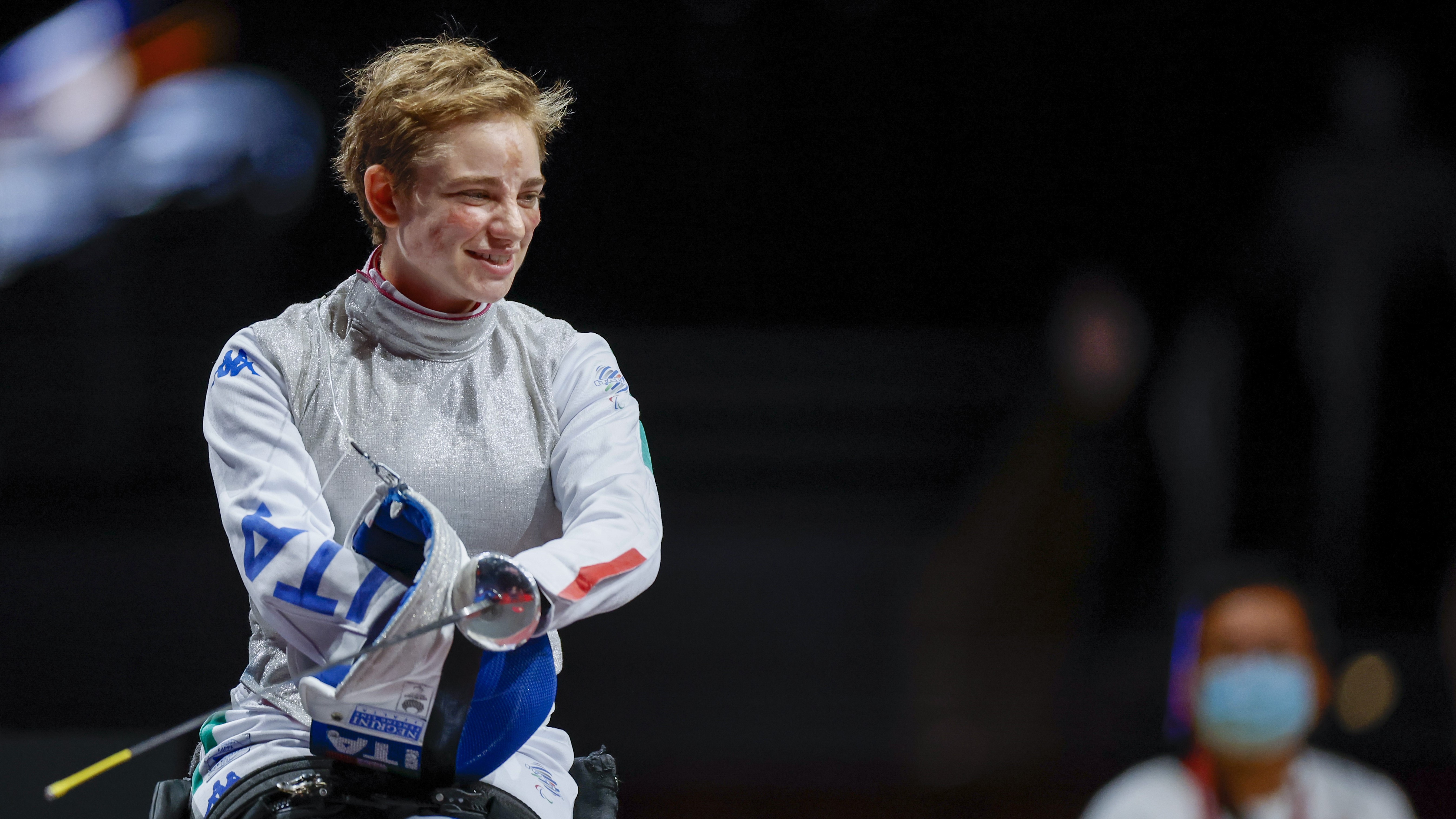 Paralympic fencer Beatrice Vio takes off her fencing mask and smiles in her fencing sports wheelchair