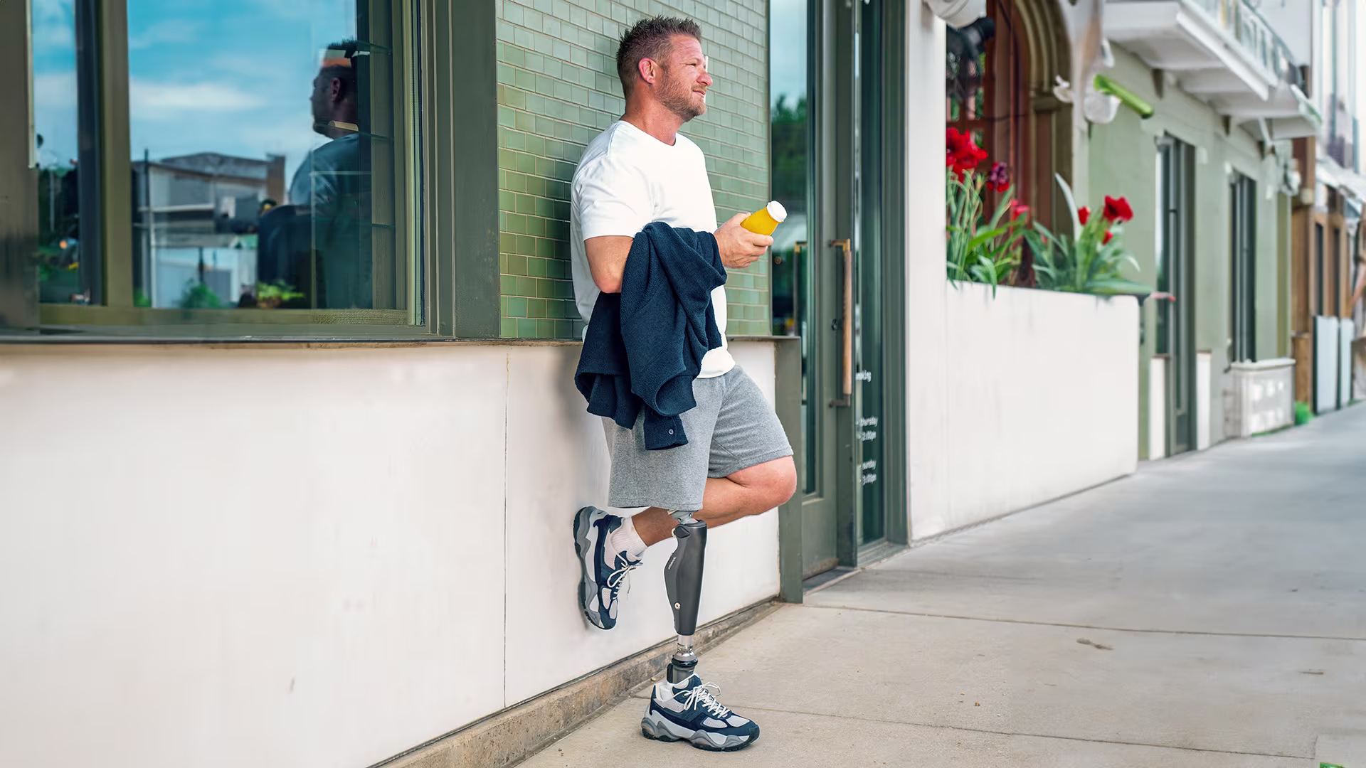 An amputee leaning against a wall, drinking his juice and wearing his Ottobock C-Leg 4.