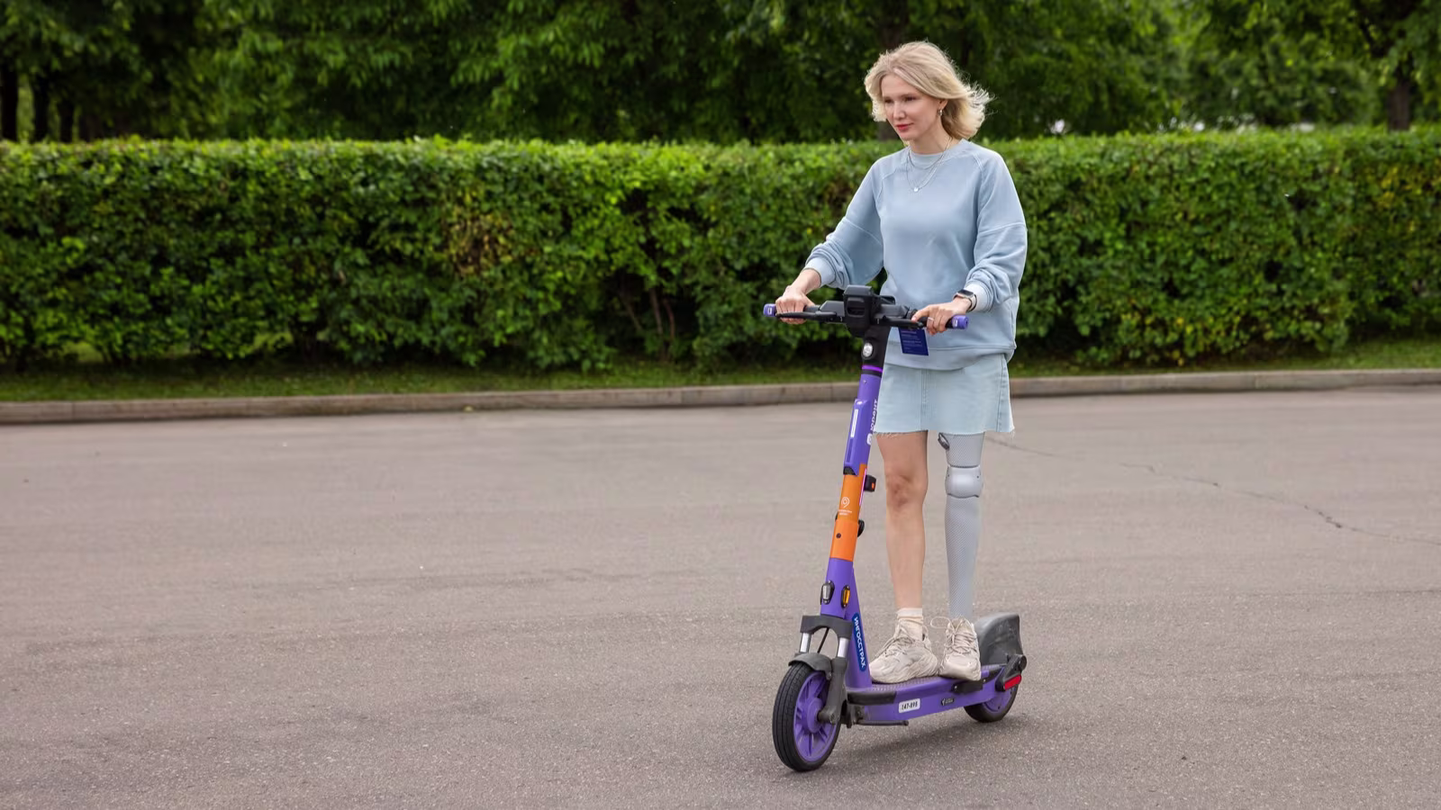 Девушка с протезом бедра катается на электросамокате.
