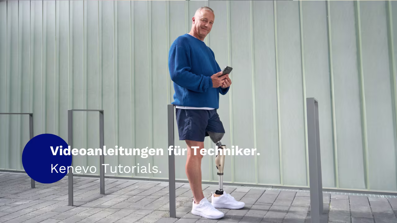 Ein amputierter Mann, der das mechatronische Kniegelenk Kenevo von Ottobock trägt, steht vor einer weißen Wand. Er hält ein Handy in der Hand und lächelt in die Kamera.