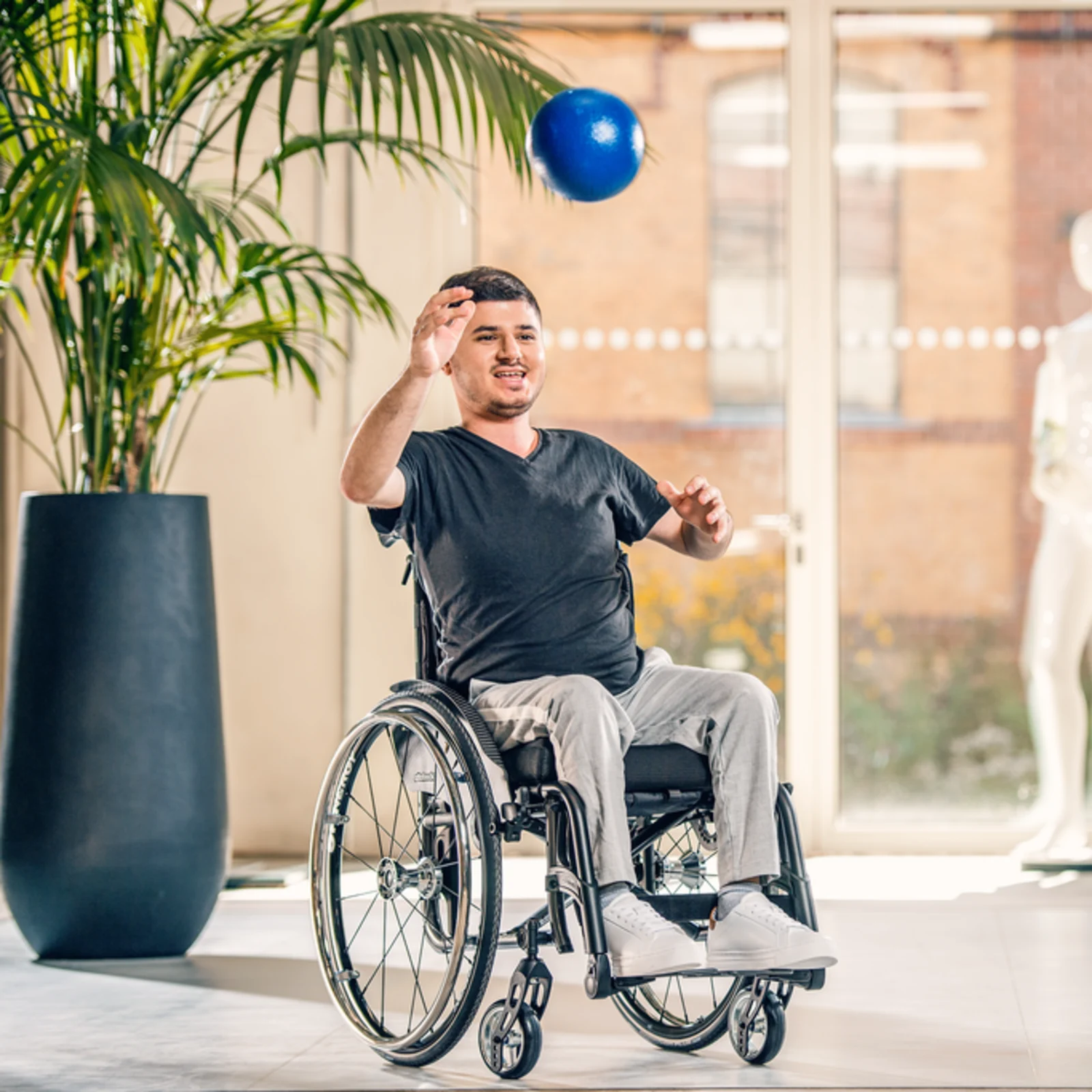 Ein Anwender sitzt im Avantgarde 4 DV Rollstuhl von Ottobock. Er wirdt seiner Physiotherapeutin einen blauen Ball zu.