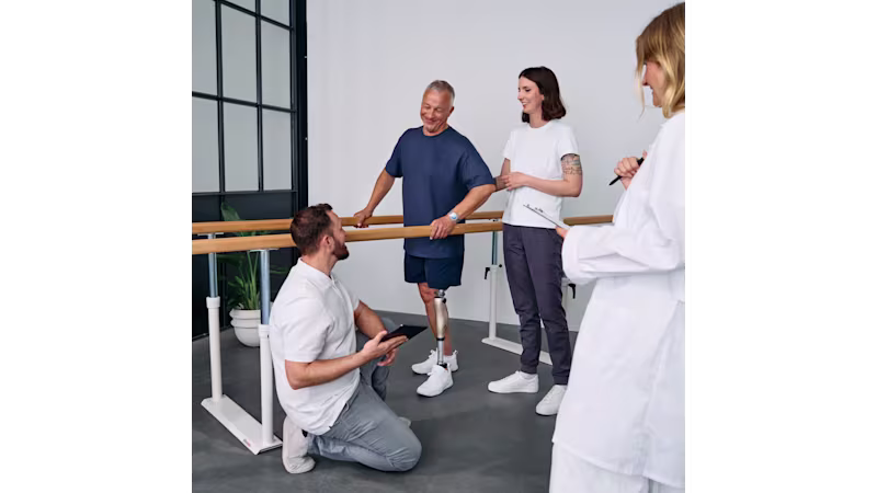 Prosthetic leg user in gait training session assisted by three Ottobock O&P specialists.