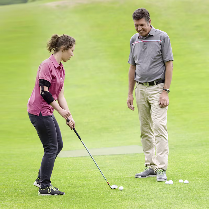 A couple plays golf outside. The woman is preparing to take her shot while wearing a custom Ottobock Omo Neurexa plus