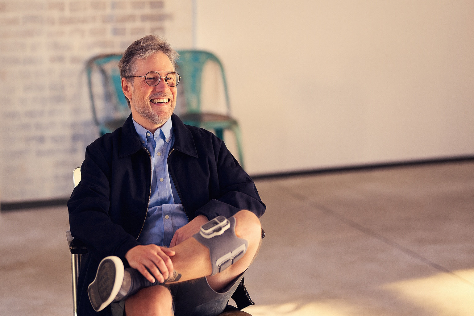 Dirk, a man recovering from a stroke, sitting relaxed in a chair, smiling and casually crossing his legs, wearing the Ottobock L300 Go on his left leg.