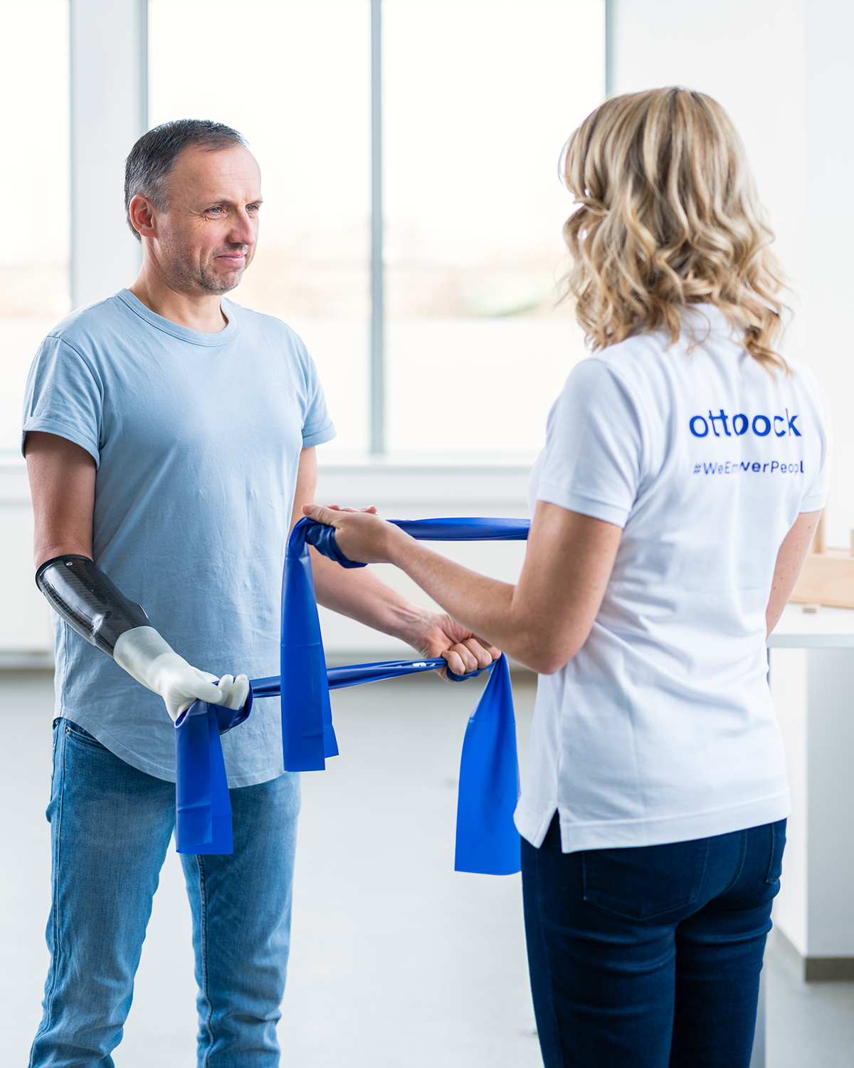 A prosthesis user and a therapist practice movements using a blue resistance band.