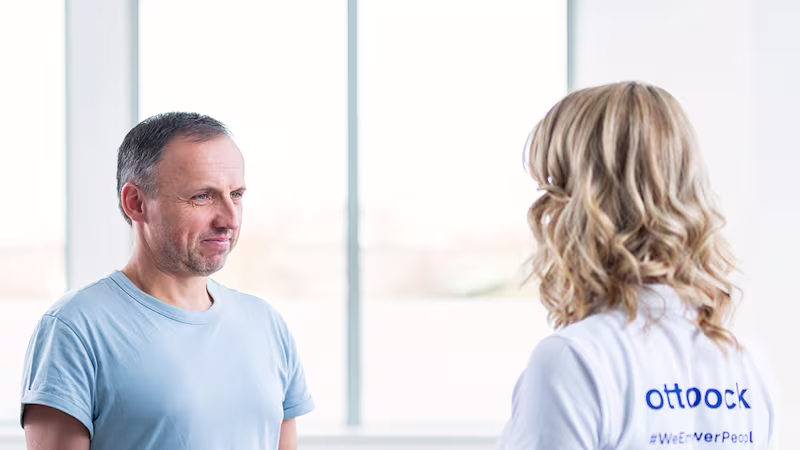 A prosthesis user and a therapist practice movements using a blue resistance band.