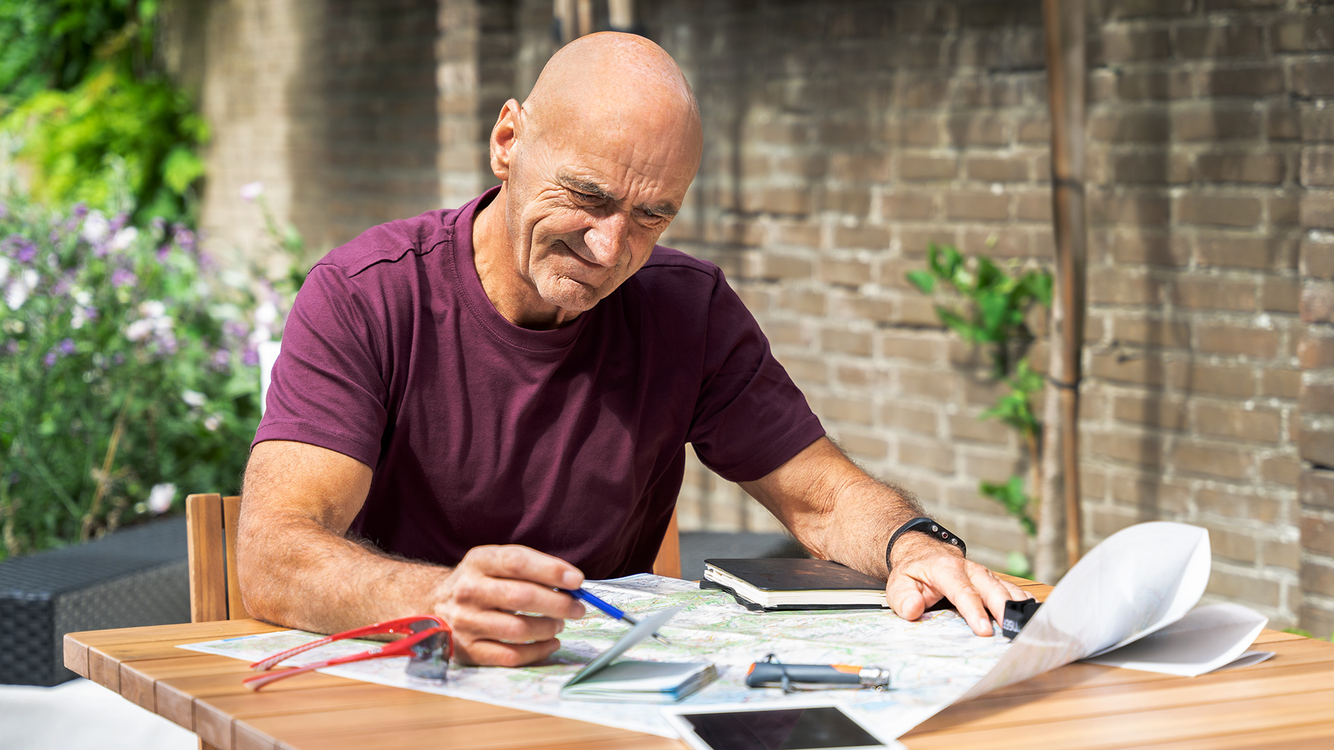 Older man with a prosthetic leg sitting outdoors at a table, studying a map and planning a trip with focus and concentration.