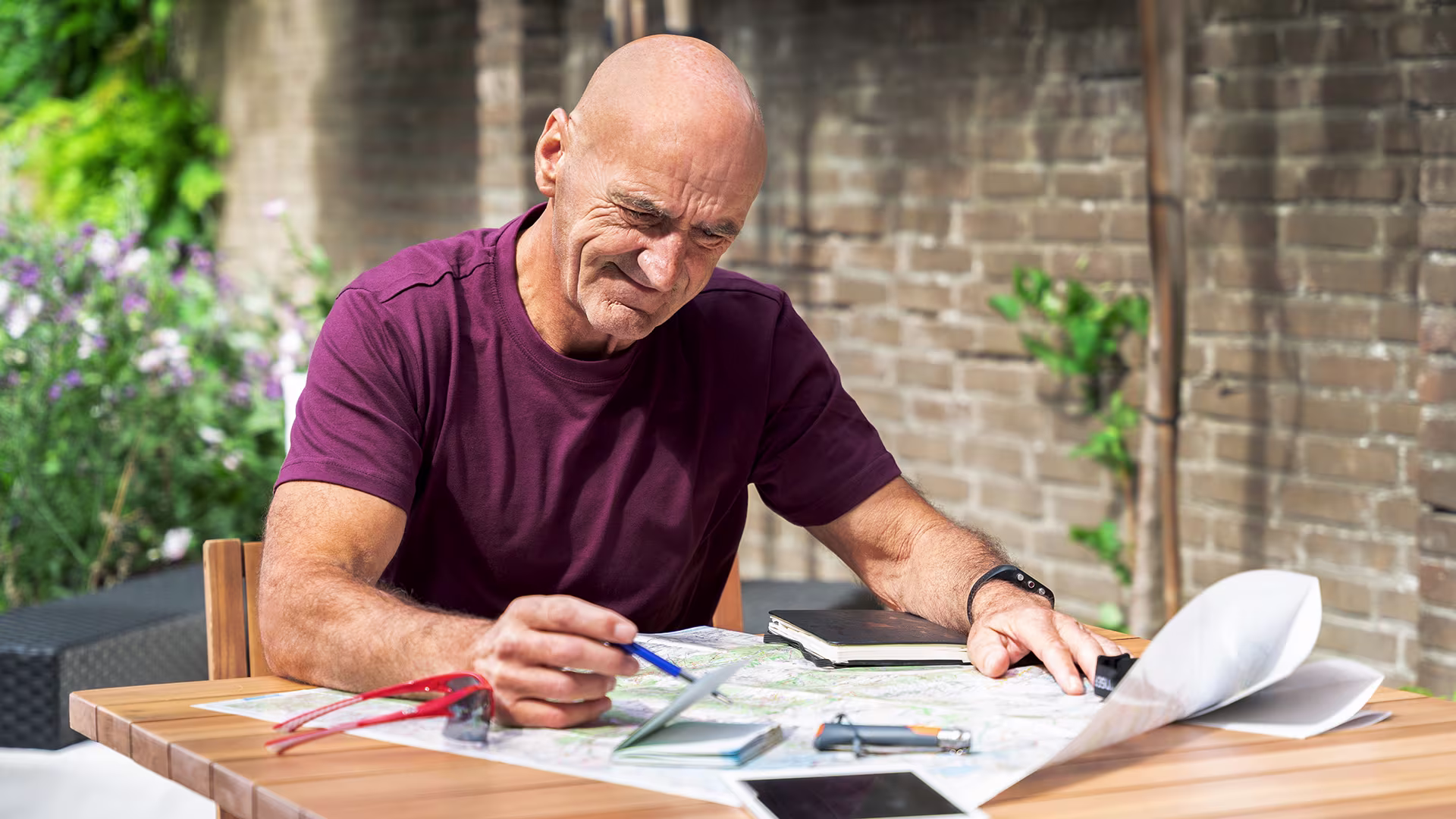 Older man with a prosthetic leg sitting outdoors at a table, studying a map and planning a trip with focus and concentration.