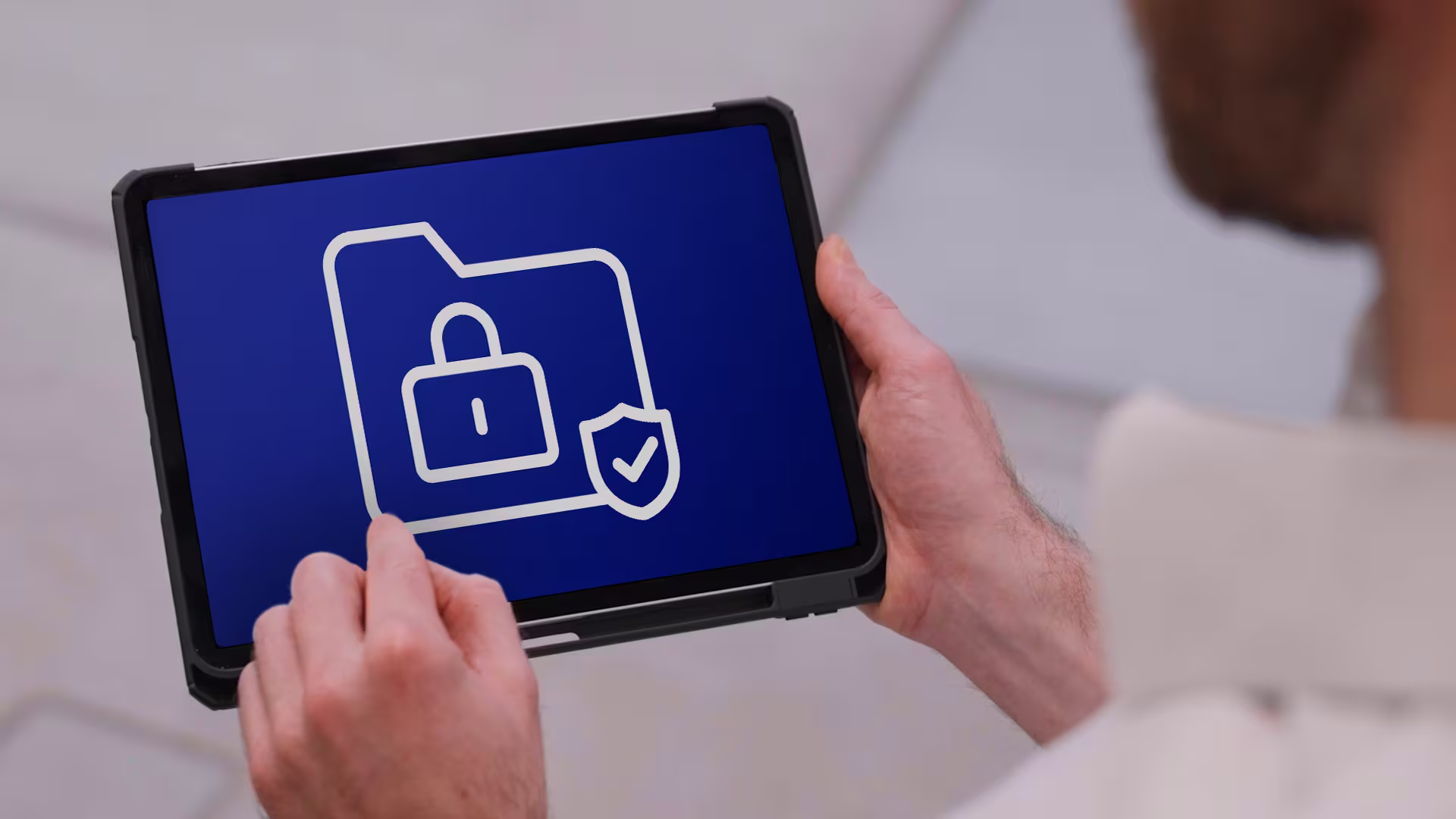 Over-the-shoulder view of a person holding a tablet displaying a white data security icon on a blue background