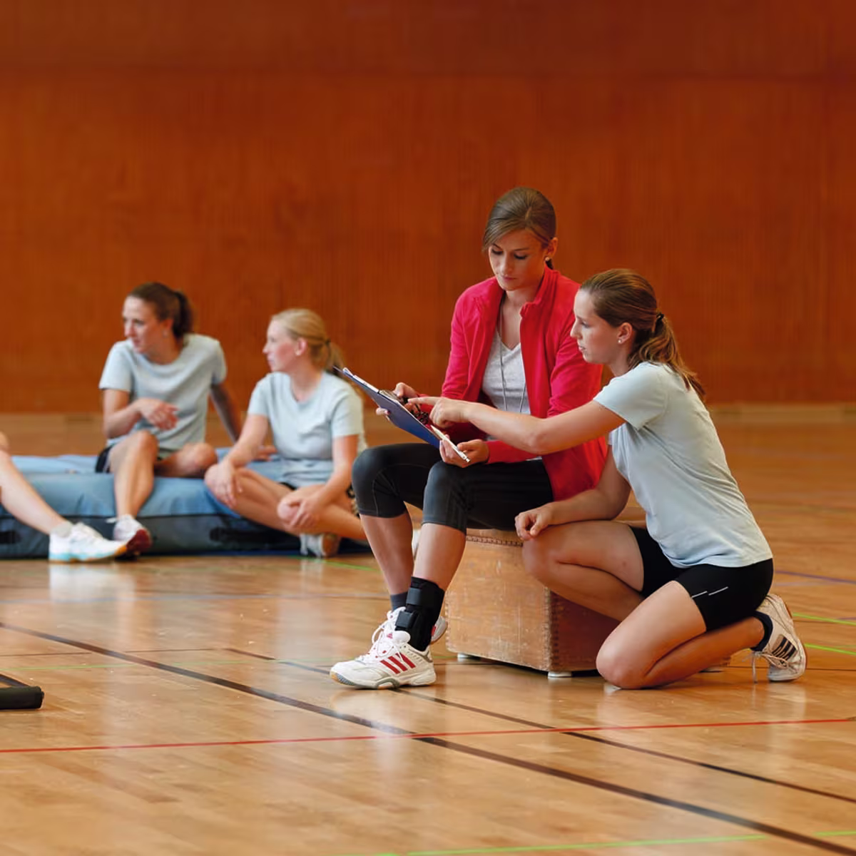 Zwei weiblich gelesene Frauen sitzen in einer Sporthalle und bereiten sich auf ein Volleyballspiel vor. Dabei trägt die linke Frau eine Malleo Tristep von Ottobock um ihr Sprunggelenk zu stabilisieren.