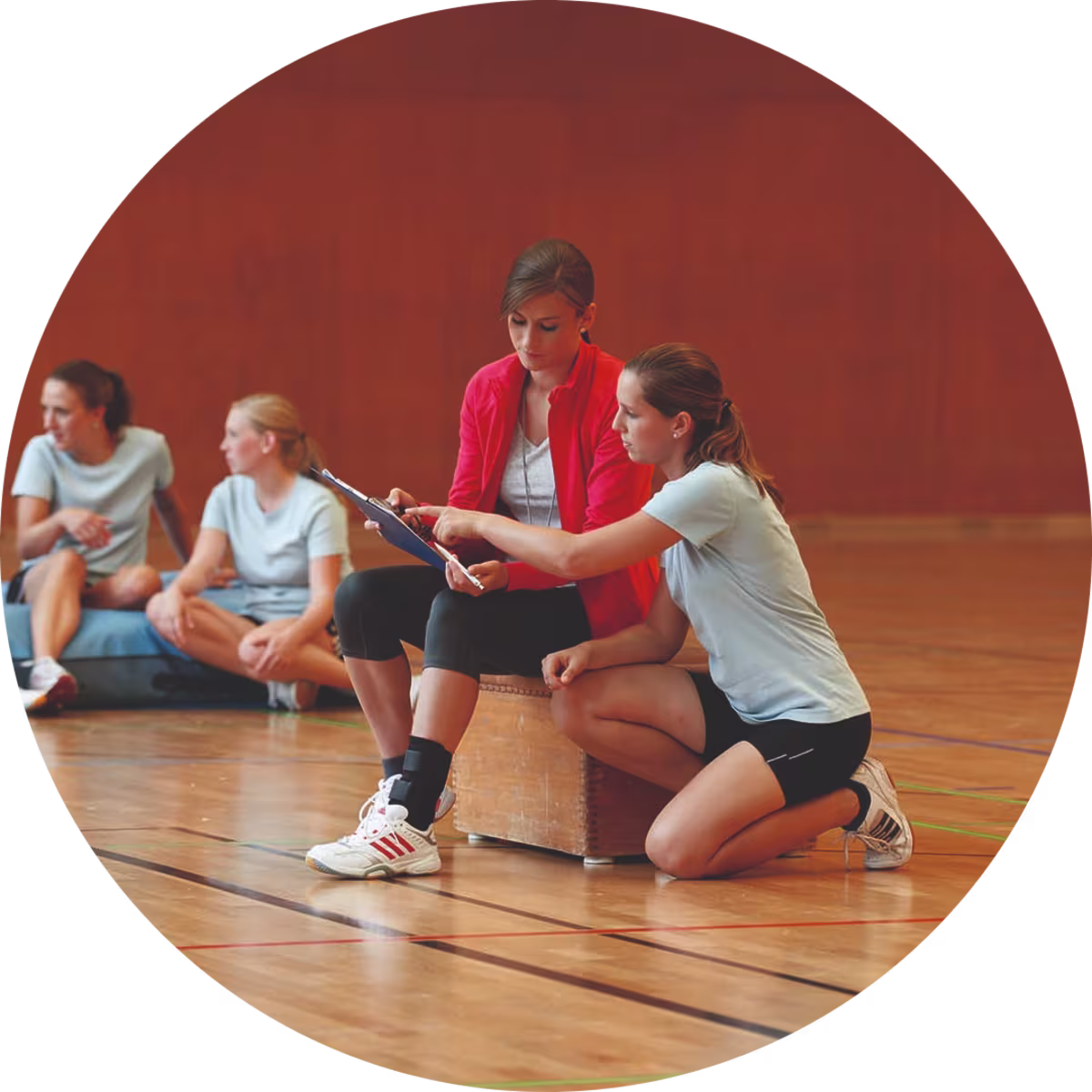 Zwei weiblich gelesene Frauen sitzen in einer Sporthalle und bereiten sich auf ein Volleyballspiel vor. Dabei trägt die linke Frau eine Malleo Tristep von Ottobock um ihr Sprunggelenk zu stabilisieren.