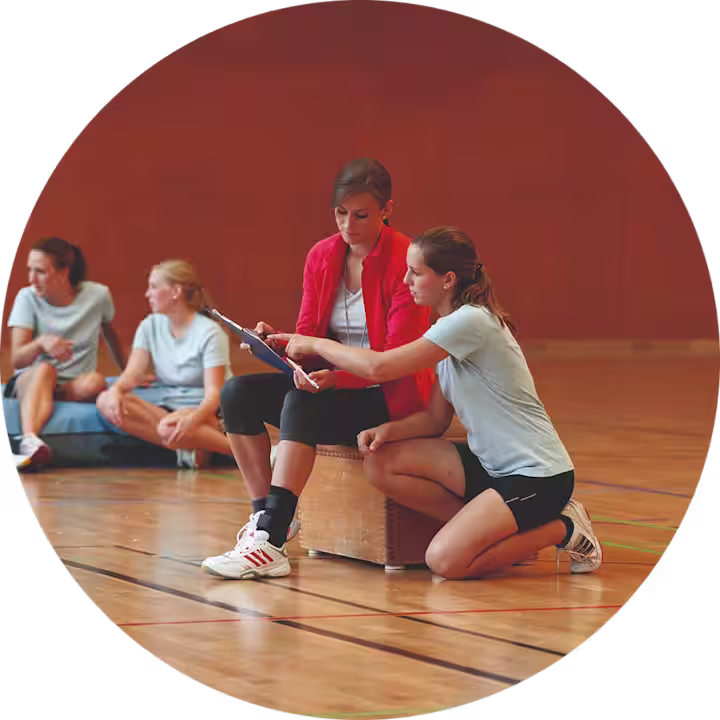 Zwei weiblich gelesene Frauen sitzen in einer Sporthalle und bereiten sich auf ein Volleyballspiel vor. Dabei trägt die linke Frau eine Malleo Tristep von Ottobock um ihr Sprunggelenk zu stabilisieren.