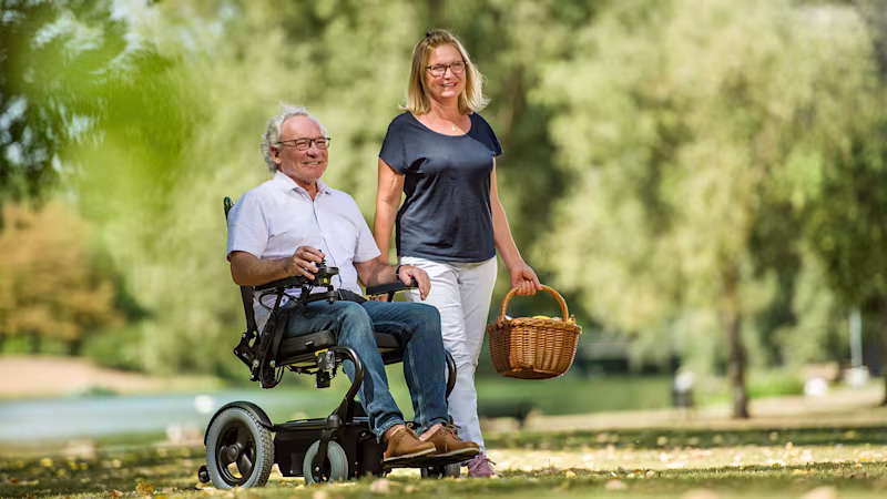 A male person drives through a green park with his Wingus power wheelchair.