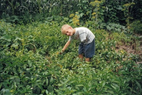 Childhood photo of Andreas Onea as a young boy standing in a lush garden, smiling at the camera.