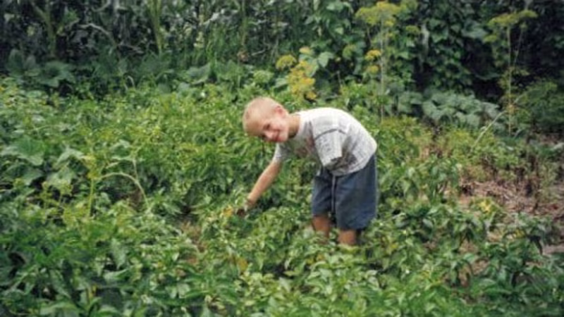 Childhood photo of Andreas Onea as a young boy standing in a lush garden, smiling at the camera.