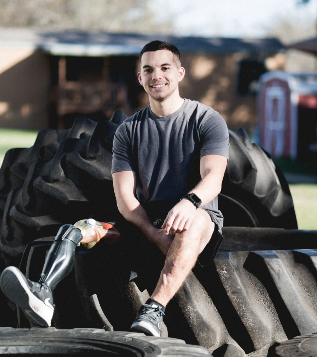 A male disabled veteran sits on a pile of tire obstacles and shows off his Ottobock prosthetic leg.