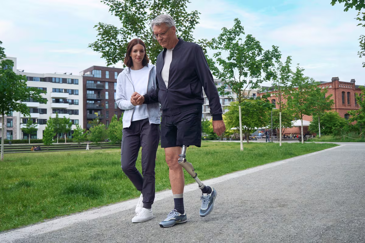 A prosthetic leg user accompanied by a prosthetic clinician walking on an outdoor path