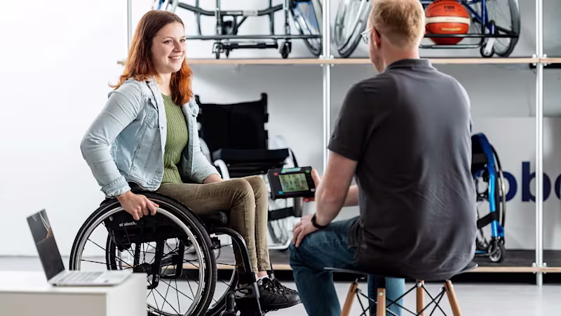 Eine Techniker berät eine Anwenderin zu Rollstühlen von Ottobock. Die Anwenderin sitzt in einem Rollstuhl vor dem Techniker.