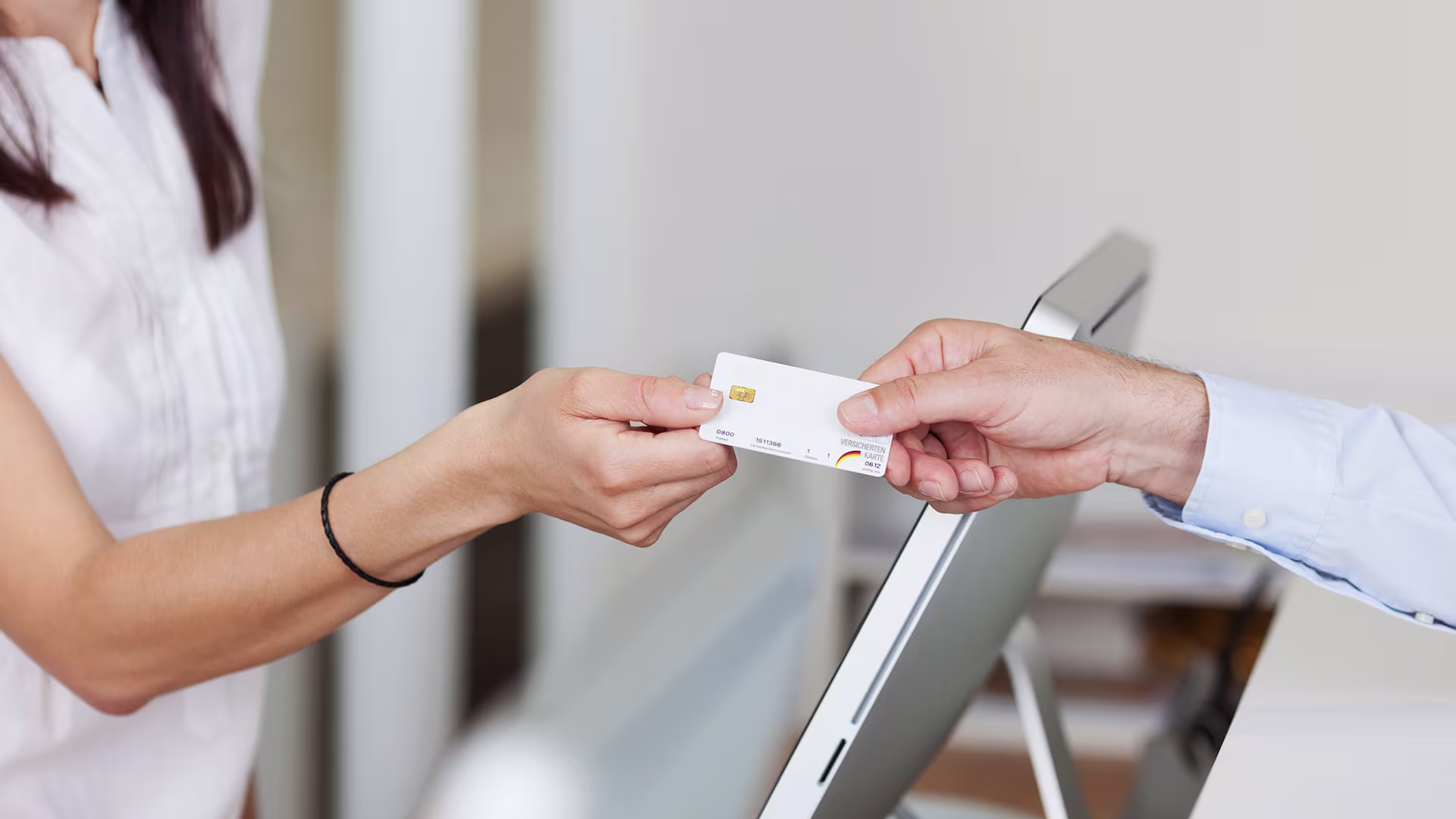 Female patient hands her insurance card to the receptionist at a medical clinic.