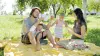 Eine Familie picknickt auf einer Wiese, dabei spielen sie Karten. Der Vater hält Spielkarten auf der Hand und trägt dabei die Michelangelo Hand