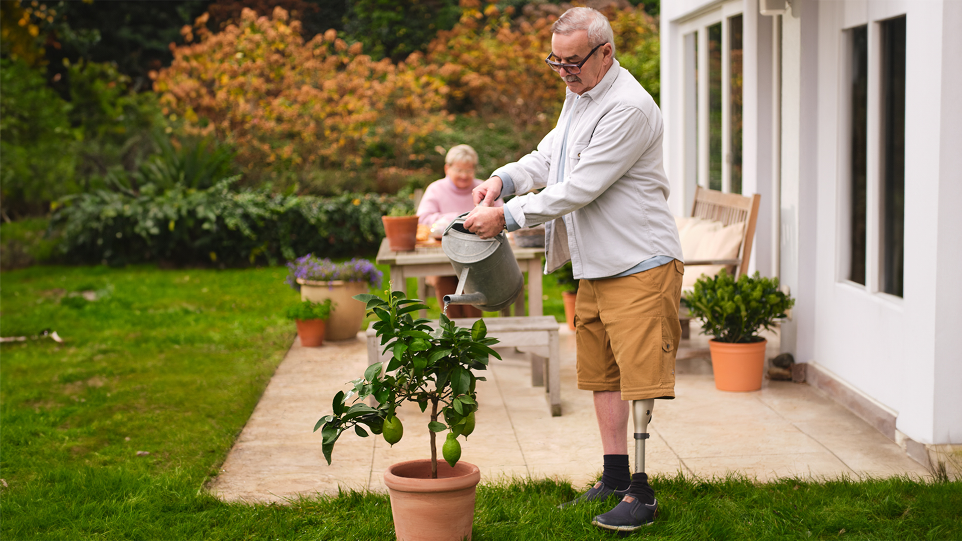 An elderly man watering his outdoor plants while wearing his Kenevo Microprocessor-Controlled Knee prosthesis