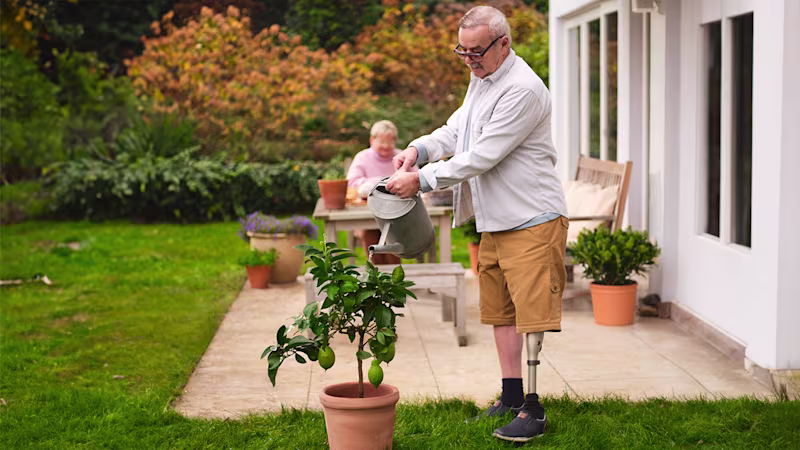 An elderly man watering his outdoor plants while wearing his Kenevo Microprocessor-Controlled Knee prosthesis